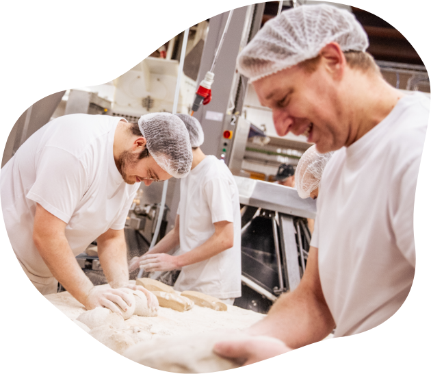 Drei Bäcker, von den Jahren 23-42, kneten in Arbeitskleidung Teiglinge in der Produktion.
